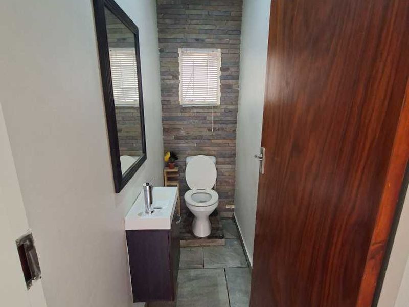 A compact guest bathroom featuring a modern wall-mounted vanity, toilet, and a stylish stone veneer feature wall with tiled flooring.
