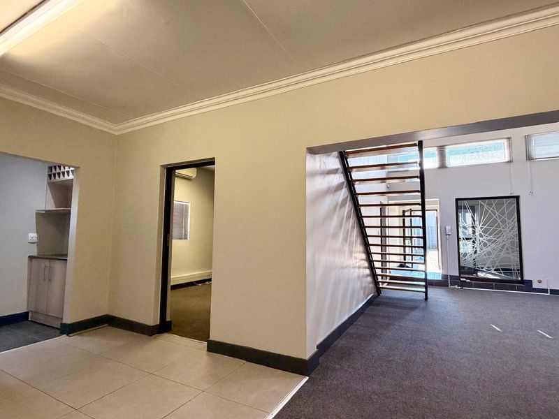 Spacious open-plan living area featuring a modern staircase, neutral finishes, and a seamless transition between tiled and carpeted flooring zones.