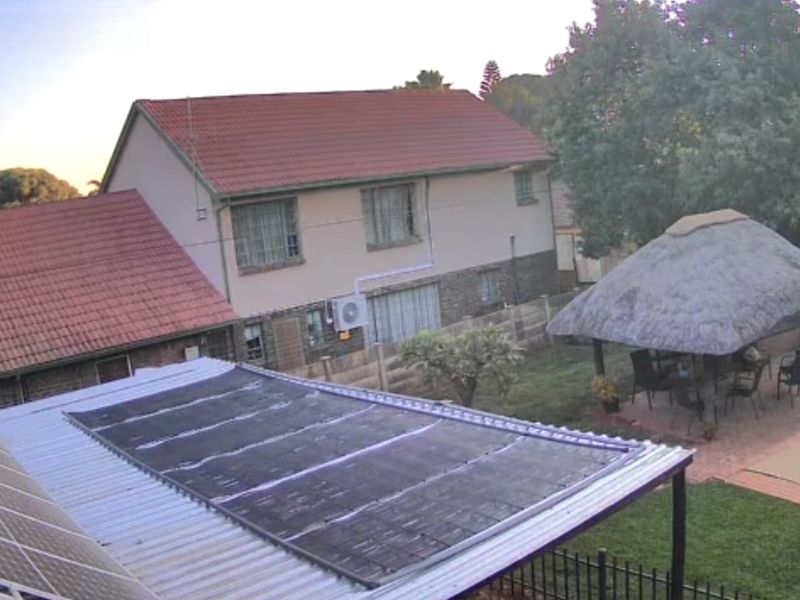 Rear view of the property featuring a swimming pool, a thatched lapa, and solar panels installed on the roof.