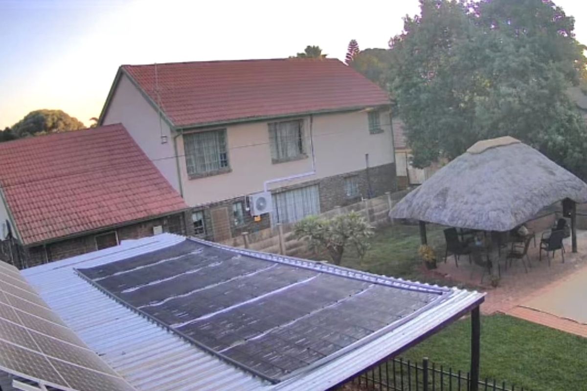 Rear view of the property featuring a swimming pool, a thatched lapa, and solar panels installed on the roof.
