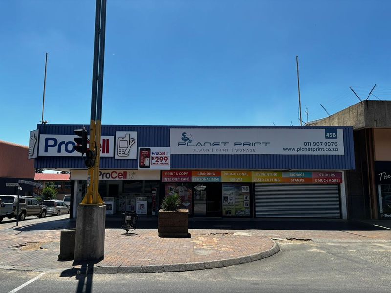 Front facade of a commercial retail property featuring prominent business signage, a metal roller shutter door, and direct street-level access.