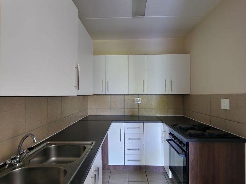 A clean and functional kitchen featuring white cabinetry, dark laminate countertops, a double bowl sink, and a built-in oven with an electric hob.