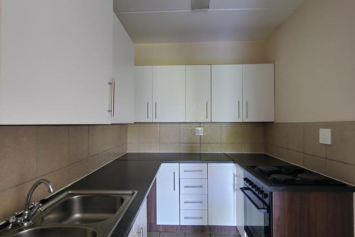 A clean and functional kitchen featuring white cabinetry, dark laminate countertops, a double bowl sink, and a built-in oven with an electric hob.