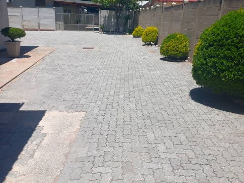 A paved driveway leading to a secure gated entrance, featuring precast concrete boundary walls and established garden shrubs.
