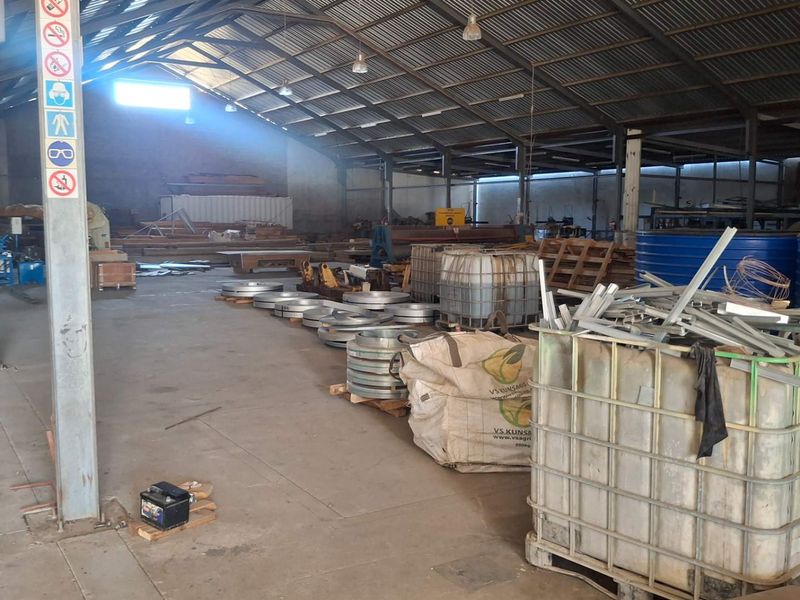 Spacious industrial warehouse featuring a steel portal frame structure, corrugated metal roofing, and durable concrete flooring, suitable for storage or manufacturing operations.