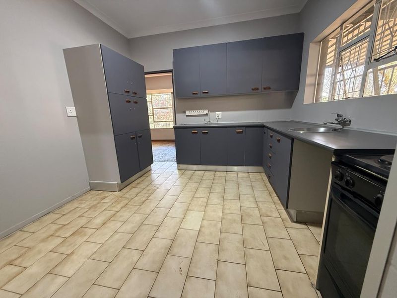 A functional kitchen featuring grey built-in cabinetry, laminate countertops, a stainless steel sink, and tiled flooring, offering a clean and practical workspace.