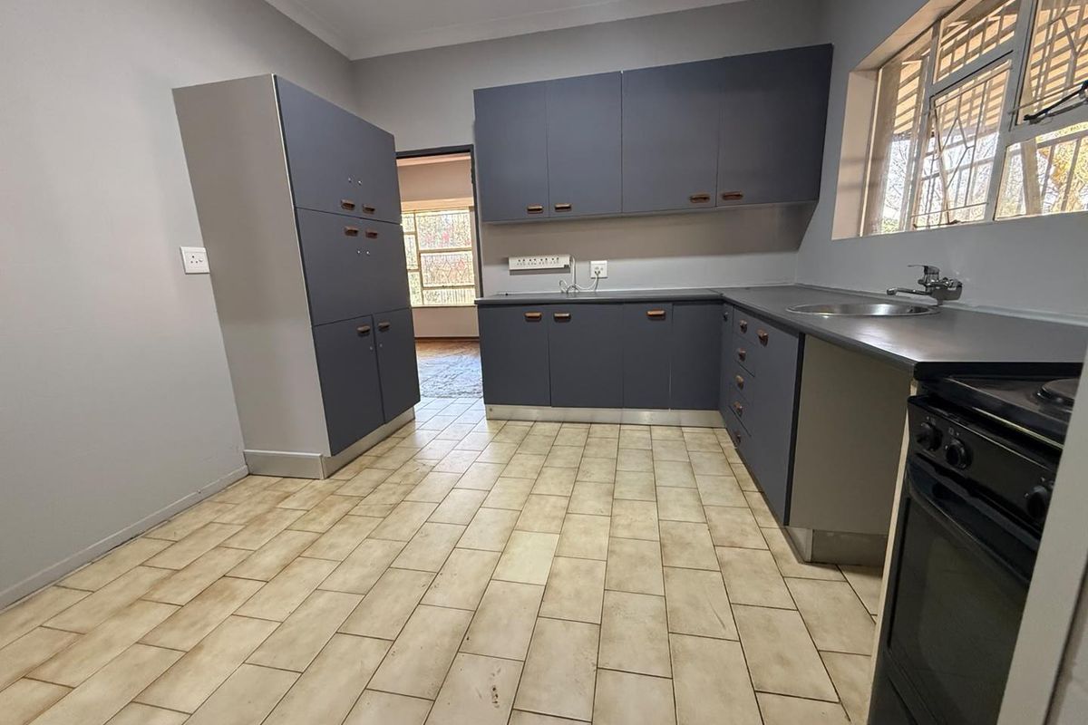 A functional kitchen featuring grey built-in cabinetry, laminate countertops, a stainless steel sink, and tiled flooring, offering a clean and practical workspace.