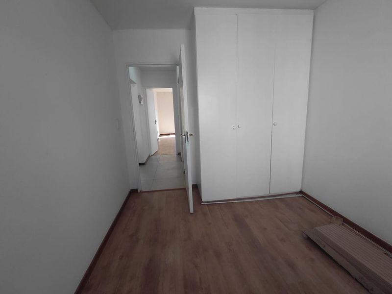 An empty bedroom featuring laminate flooring and a built-in wardrobe, with a doorway leading to an adjacent hallway.