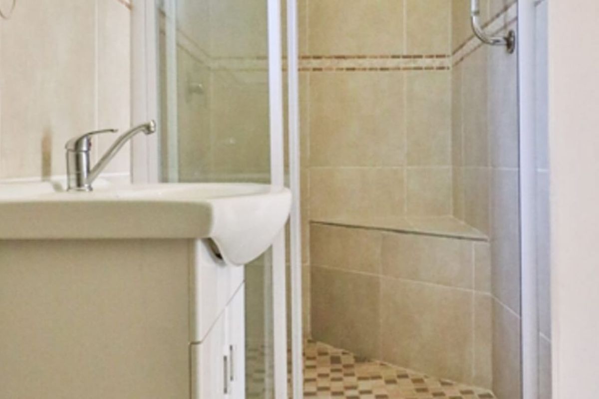 A functional bathroom featuring a vanity basin with a mixer tap and a tiled shower enclosure with a built-in bench seat.