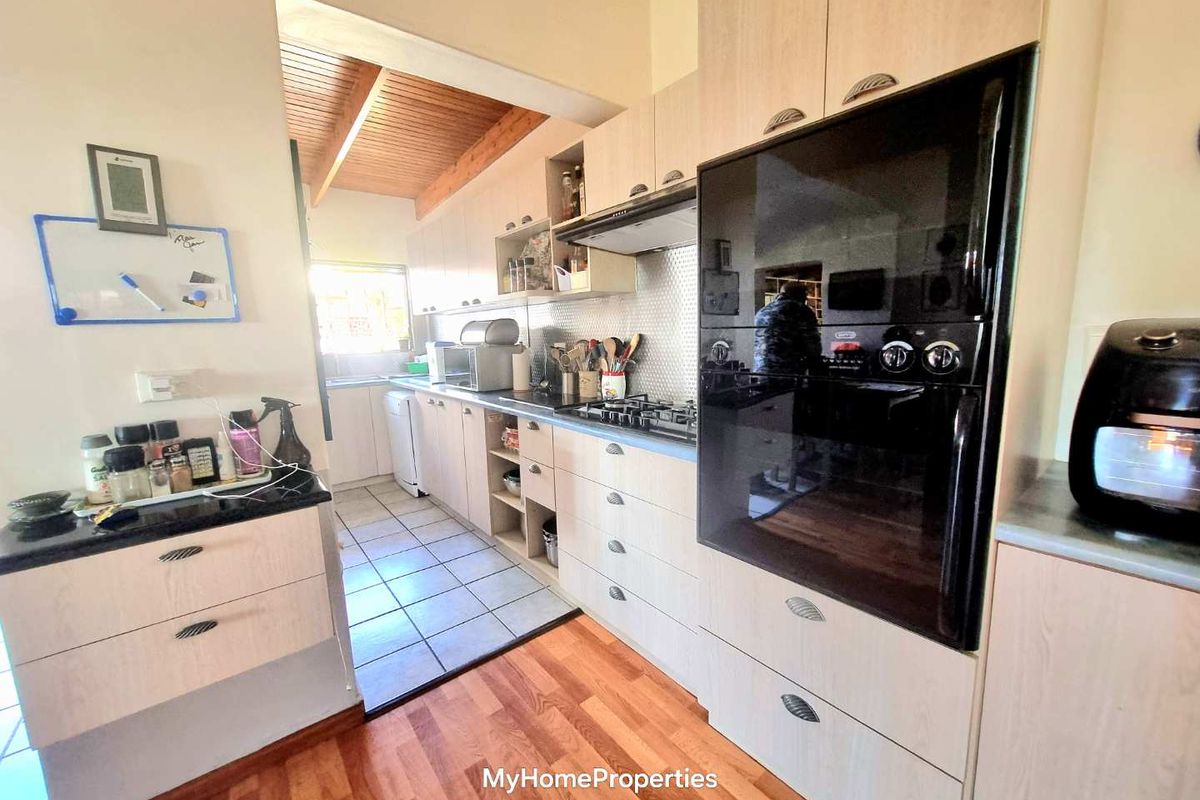 A functional kitchen featuring light wood cabinetry, a built-in oven, gas hob, extractor fan, and a combination of tiled and wooden flooring.