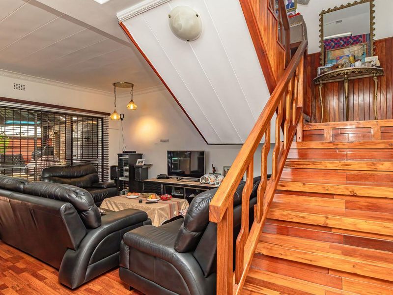 Spacious living room featuring warm wooden flooring, a prominent wooden staircase with balustrade, and large sliding glass doors leading to the outdoor area.