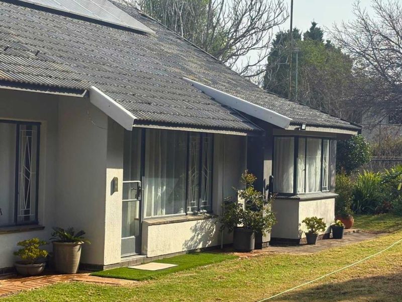 Rear view of the house featuring a corrugated roof with solar panels, metal-framed windows, and a paved walkway leading onto the garden lawn.