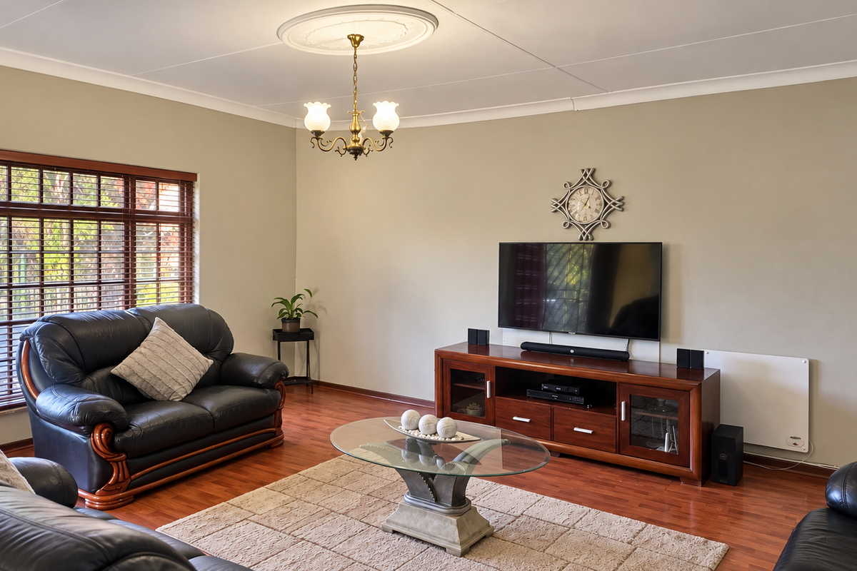 Spacious living room featuring warm laminate flooring, classic ceiling rose with chandelier, and large windows with timber frames.