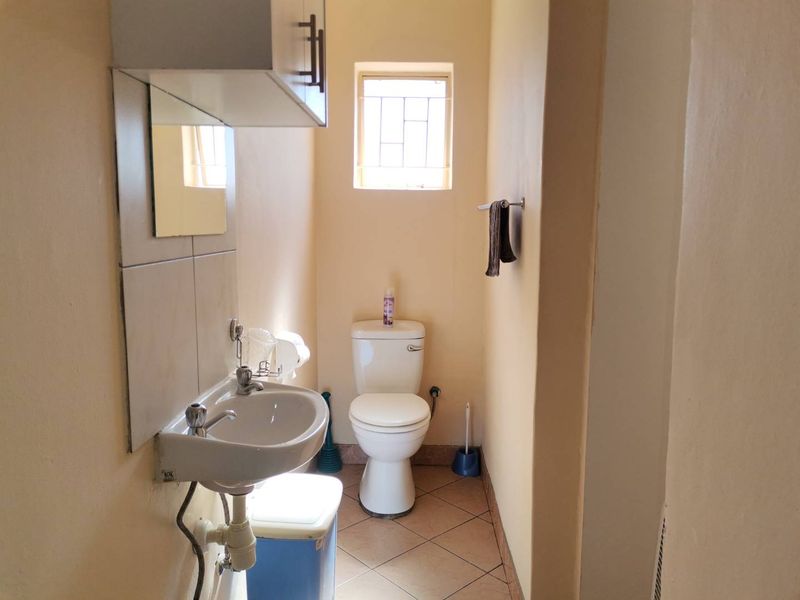 A functional guest bathroom featuring a pedestal basin, toilet, tiled flooring, and a wall-mounted storage cabinet.