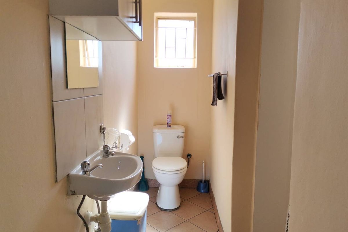 A functional guest bathroom featuring a pedestal basin, toilet, tiled flooring, and a wall-mounted storage cabinet.