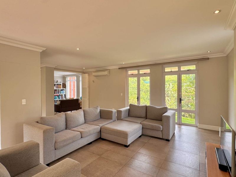 Spacious living room featuring tiled flooring, recessed lighting, crown molding, and double glass doors providing natural light and garden access.