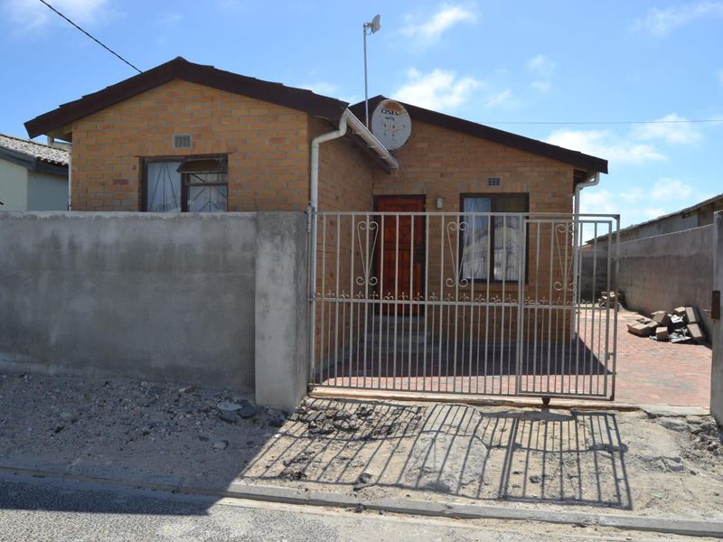 Front elevation of a face brick house featuring a metal security gate, paved driveway, and concrete boundary walling.