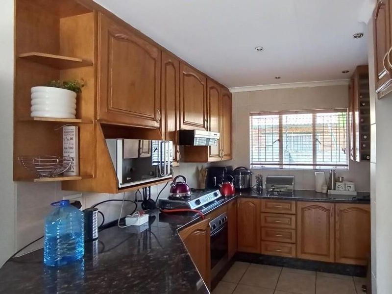 A functional kitchen featuring traditional wooden cabinetry, dark granite countertops, built-in oven, and tiled flooring with natural light from a window.