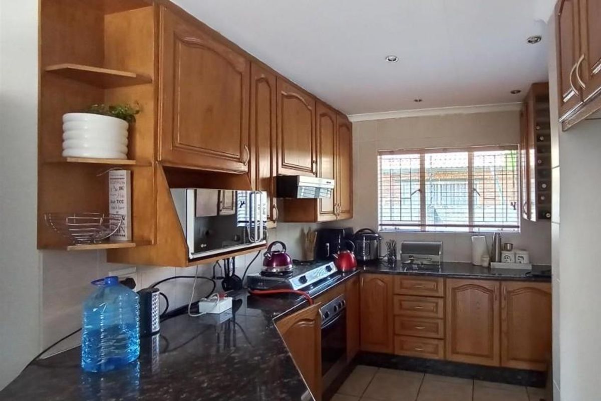 A functional kitchen featuring traditional wooden cabinetry, dark granite countertops, built-in oven, and tiled flooring with natural light from a window.