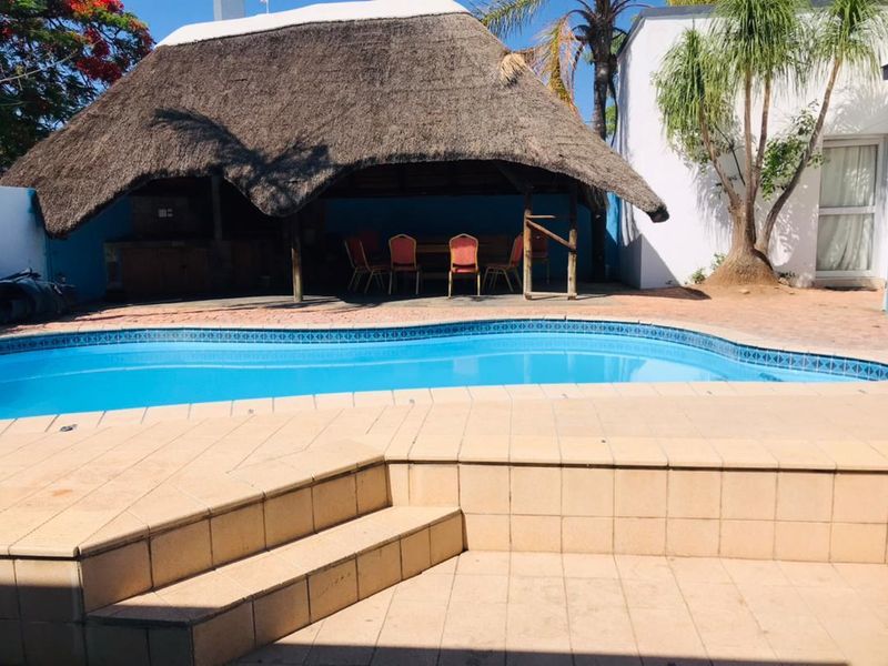 Outdoor pool area featuring a swimming pool, tiled surround, and a thatched lapa with a built-in braai, ideal for outdoor entertainment.