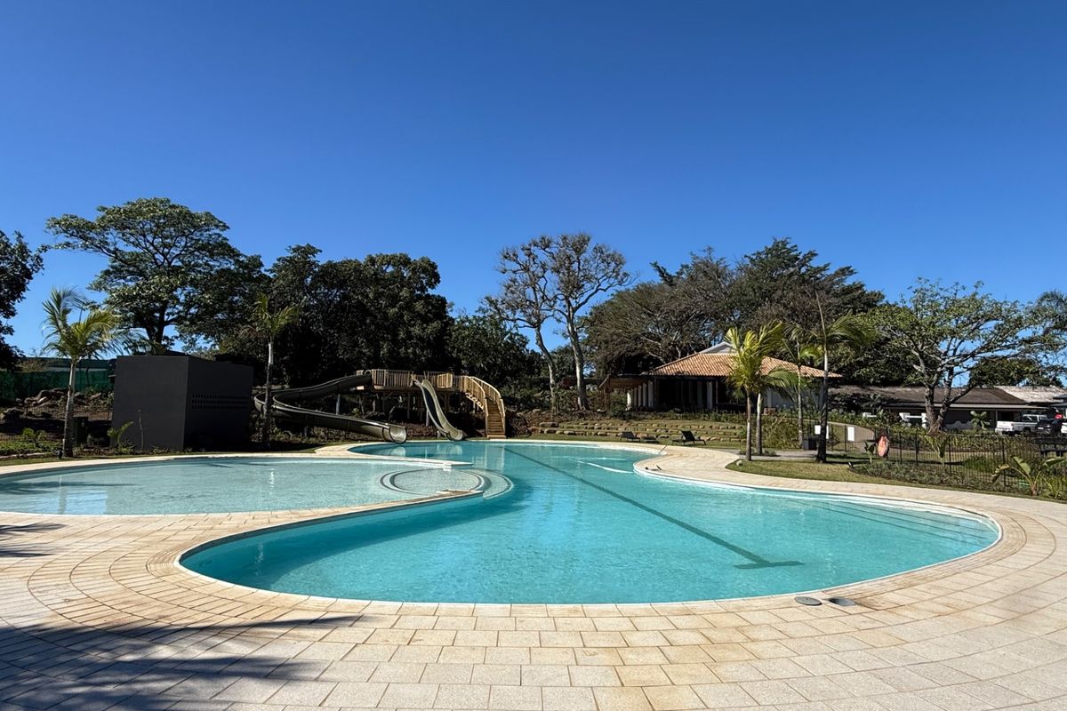 A well-maintained swimming pool area featuring a water slide, paved decking, and surrounding landscaped gardens in a peaceful outdoor setting.