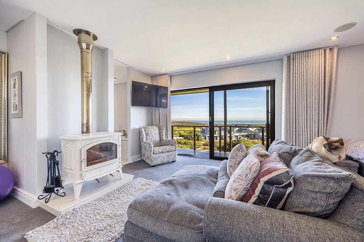 A bright living room featuring a freestanding fireplace, recessed ceiling lighting, and large sliding glass doors opening to a balcony with scenic coastal views.