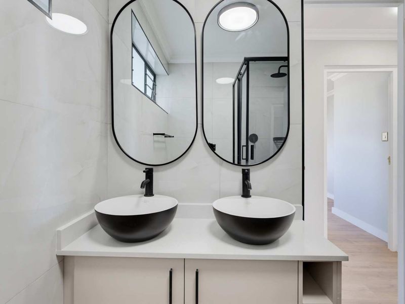 Modern bathroom featuring a double vanity with vessel sinks, black matte fixtures, oval mirrors, and a glass-enclosed shower with contemporary wall tiling.