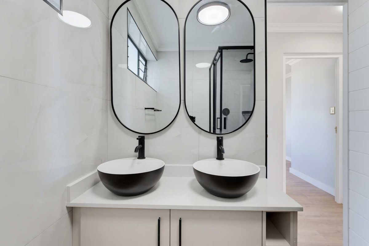 Modern bathroom featuring a double vanity with vessel sinks, black matte fixtures, oval mirrors, and a glass-enclosed shower with contemporary wall tiling.