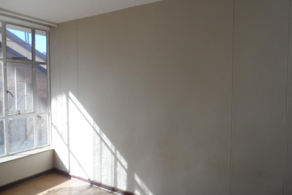 A bright, empty bedroom featuring large windows that allow for natural light, neutral wall finishes, and parquet flooring.