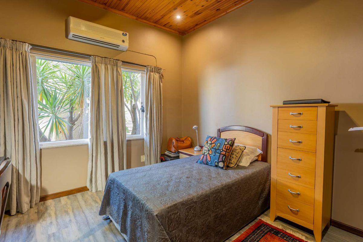 A cozy bedroom featuring timber ceiling paneling, laminate flooring, and a wall-mounted split-system air conditioning unit.