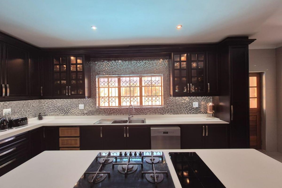Modern kitchen featuring dark wood cabinetry, stone countertops, mosaic tile backsplash, and a central island with integrated gas and electric hobs.