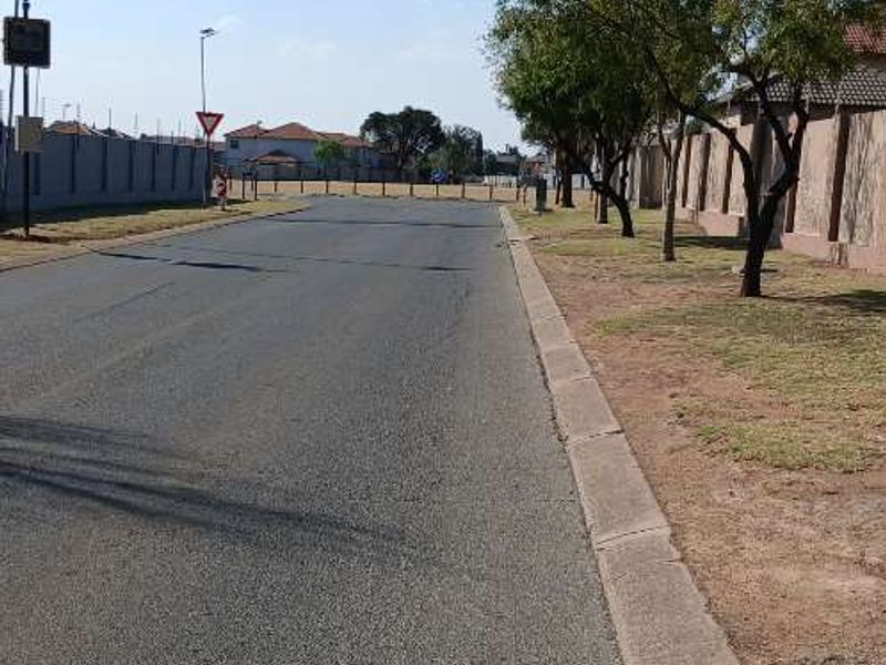 A view of the residential street approach, featuring paved asphalt road, concrete curbing, and established perimeter boundary walls.