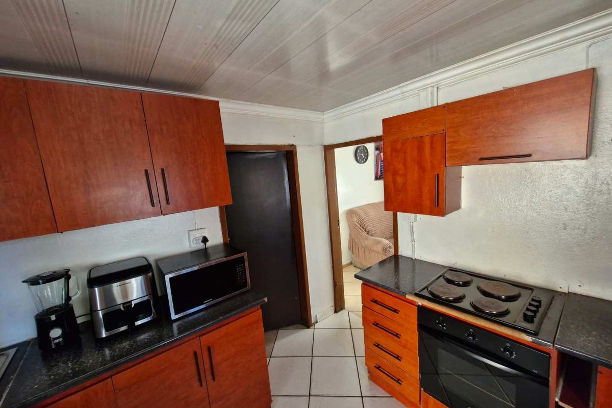 A functional kitchen featuring wood-look cabinetry, dark countertops, a built-in oven, and a hob, with tiled flooring throughout.