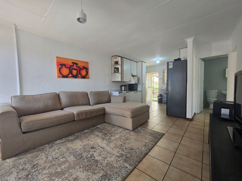 Open-plan living area featuring tiled flooring, integrated kitchen cabinetry, and direct access to an adjacent bathroom and exterior entrance.