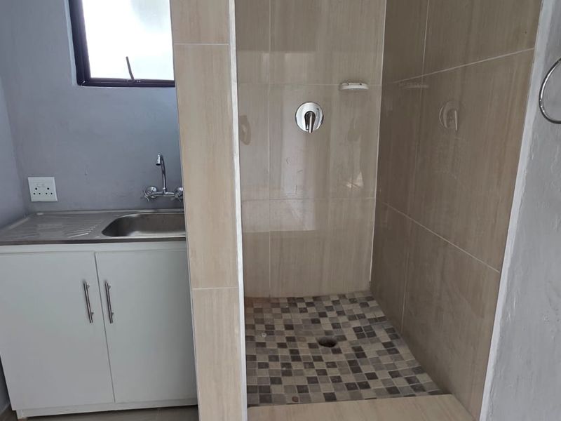 A functional bathroom featuring a tiled shower enclosure, a vanity cabinet with a stainless steel sink, and neutral wall finishes.