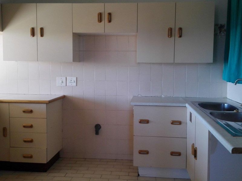 A functional kitchen space featuring built-in cabinetry, tiled splashbacks, and a stainless steel sink, offering a blank canvas for modern renovation.