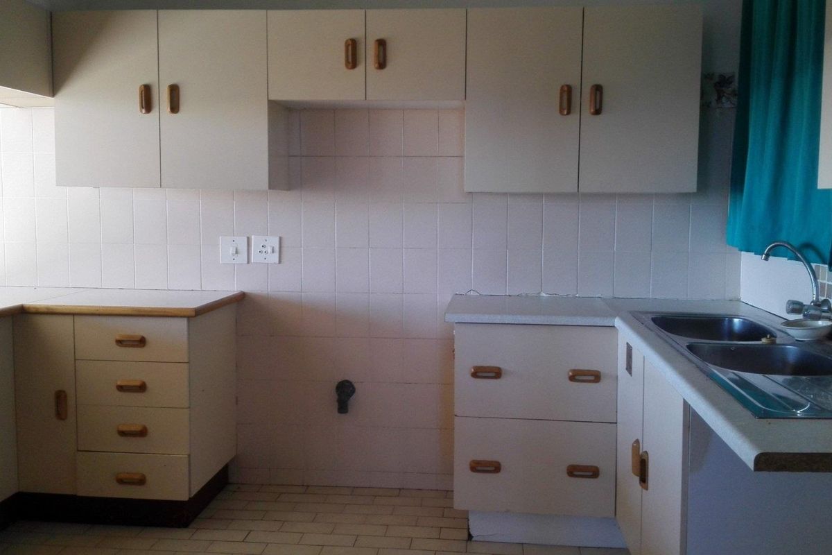 A functional kitchen space featuring built-in cabinetry, tiled splashbacks, and a stainless steel sink, offering a blank canvas for modern renovation.