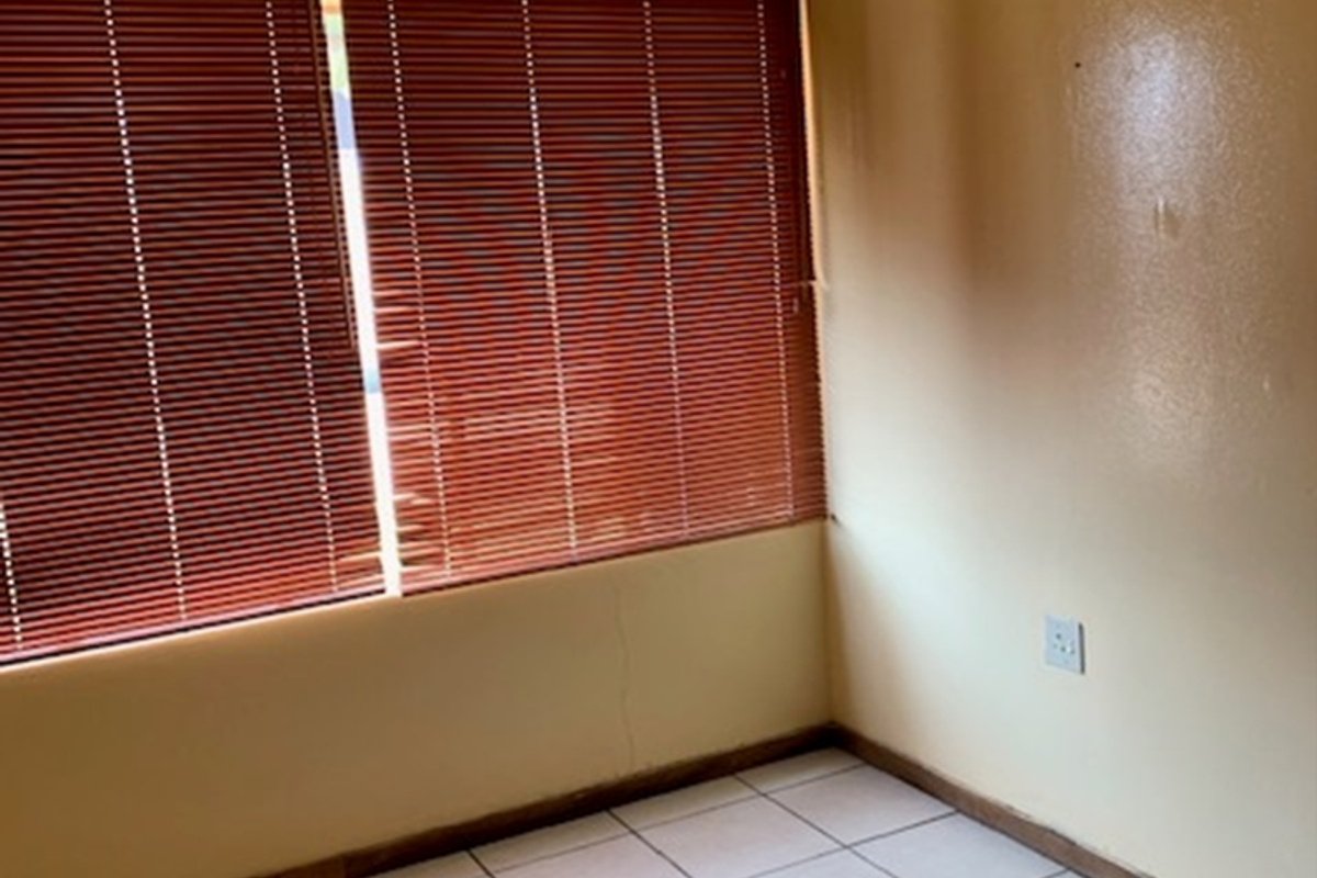 A vacant bedroom featuring tiled flooring, yellow painted walls, and fitted venetian blinds.