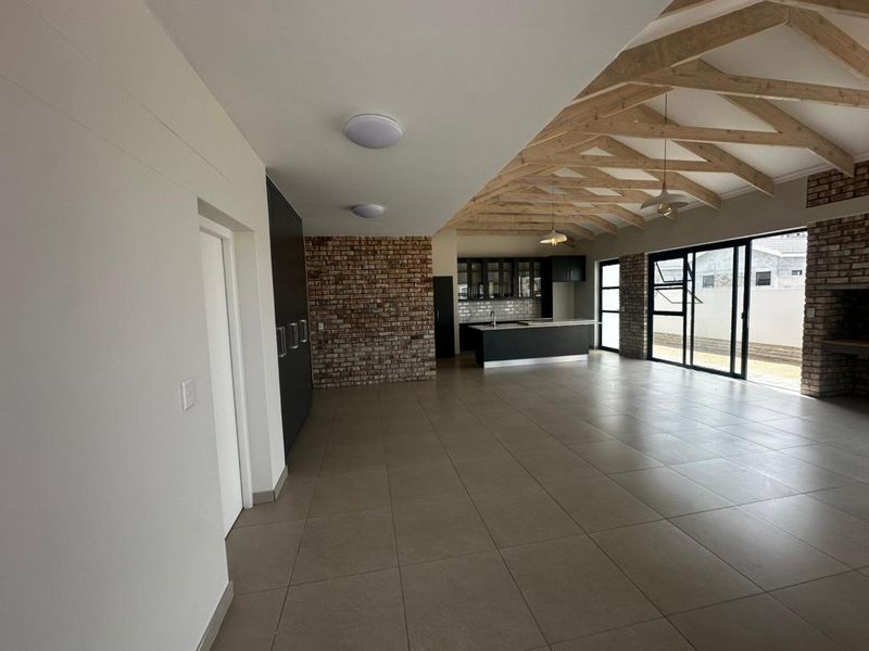 Spacious open-plan living area featuring exposed timber roof trusses, a modern kitchen with island, and large sliding doors leading to the exterior.