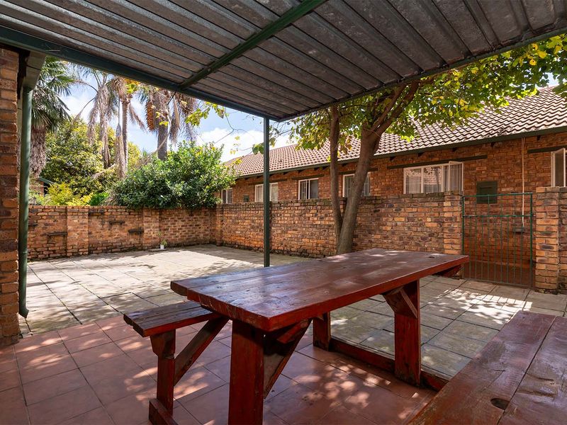 A private outdoor patio area featuring a covered seating space, paved flooring, and enclosed by traditional face-brick boundary walls.
