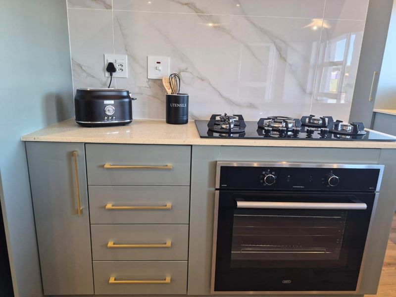 Modern kitchen section featuring a built-in oven, gas hob, stone countertop, and elegant marble-look splashback with contemporary cabinetry.