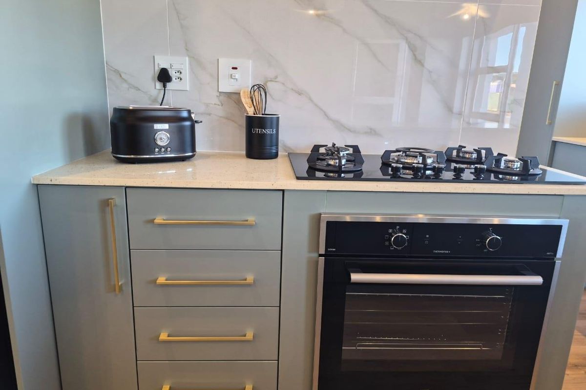 Modern kitchen section featuring a built-in oven, gas hob, stone countertop, and elegant marble-look splashback with contemporary cabinetry.