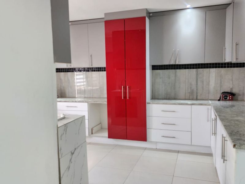 A modern kitchen featuring high-gloss red and grey cabinetry, stone countertops, and a tiled backsplash, offering a clean and functional workspace.