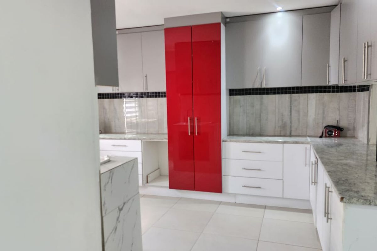 A modern kitchen featuring high-gloss red and grey cabinetry, stone countertops, and a tiled backsplash, offering a clean and functional workspace.