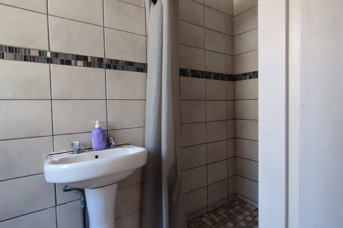 A functional bathroom featuring a pedestal basin, tiled walls with decorative mosaic accents, and a shower area with a curtain.