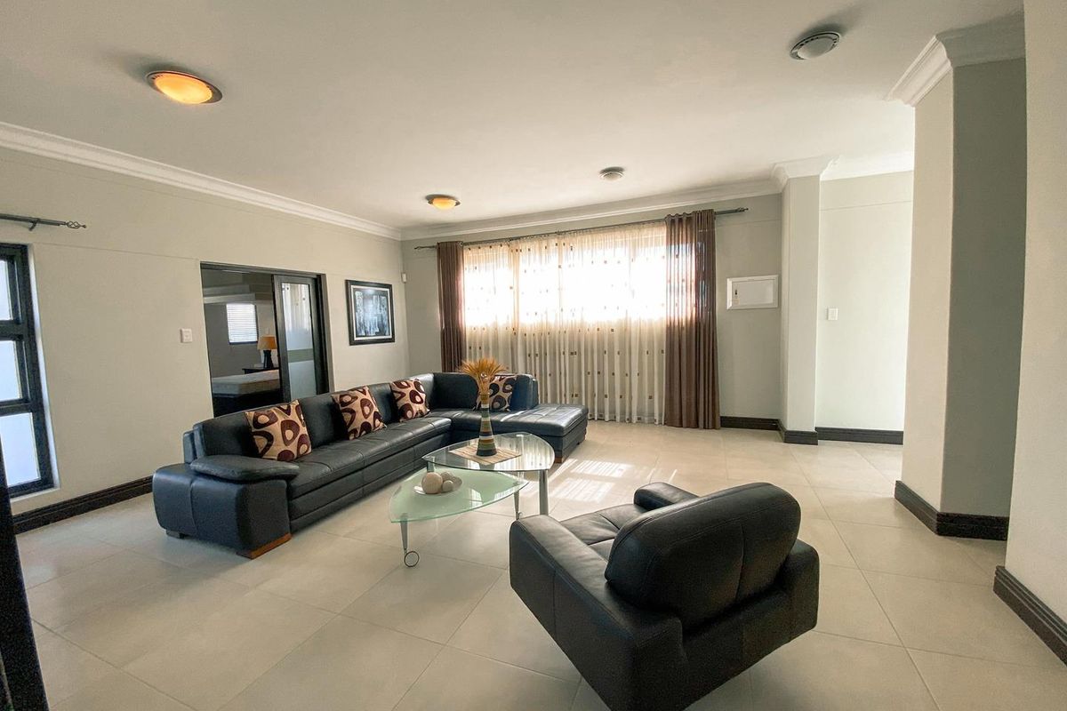 Spacious living room featuring neutral tiled flooring, crown molding, and large windows with curtains, providing a bright and open atmosphere.