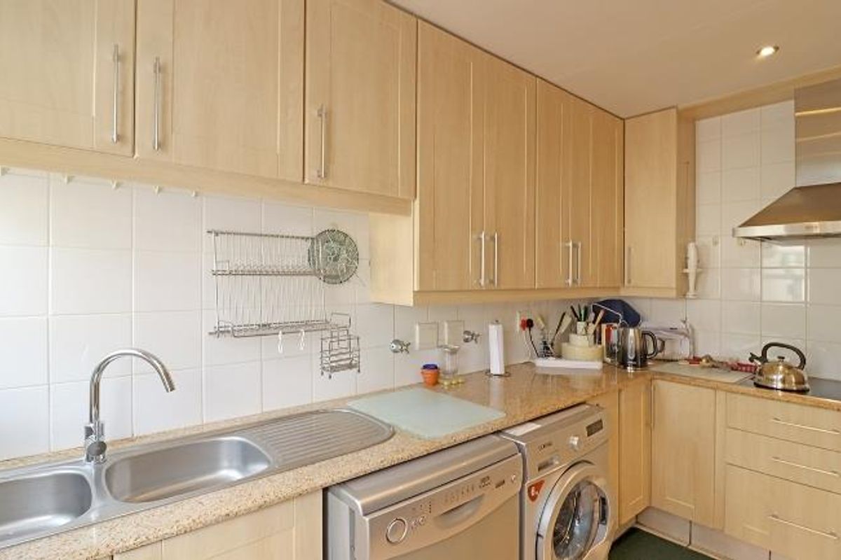 Functional kitchen featuring light wood-toned cabinetry, tiled splashbacks, stainless steel sink, and integrated space for laundry appliances.