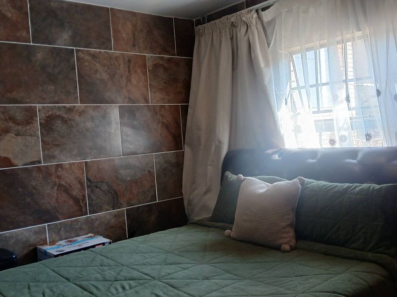 A bedroom featuring a large format tiled accent wall and a window fitted with security bars.