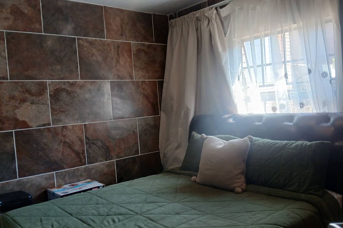 A bedroom featuring a large format tiled accent wall and a window fitted with security bars.