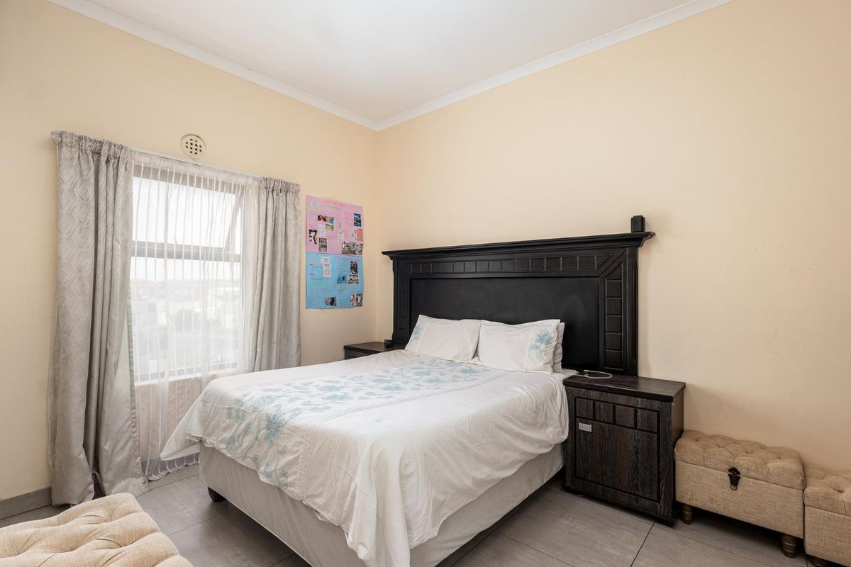 A well-lit bedroom featuring neutral wall tones, tiled flooring, and a window with sheer curtains, providing a comfortable and functional living space.